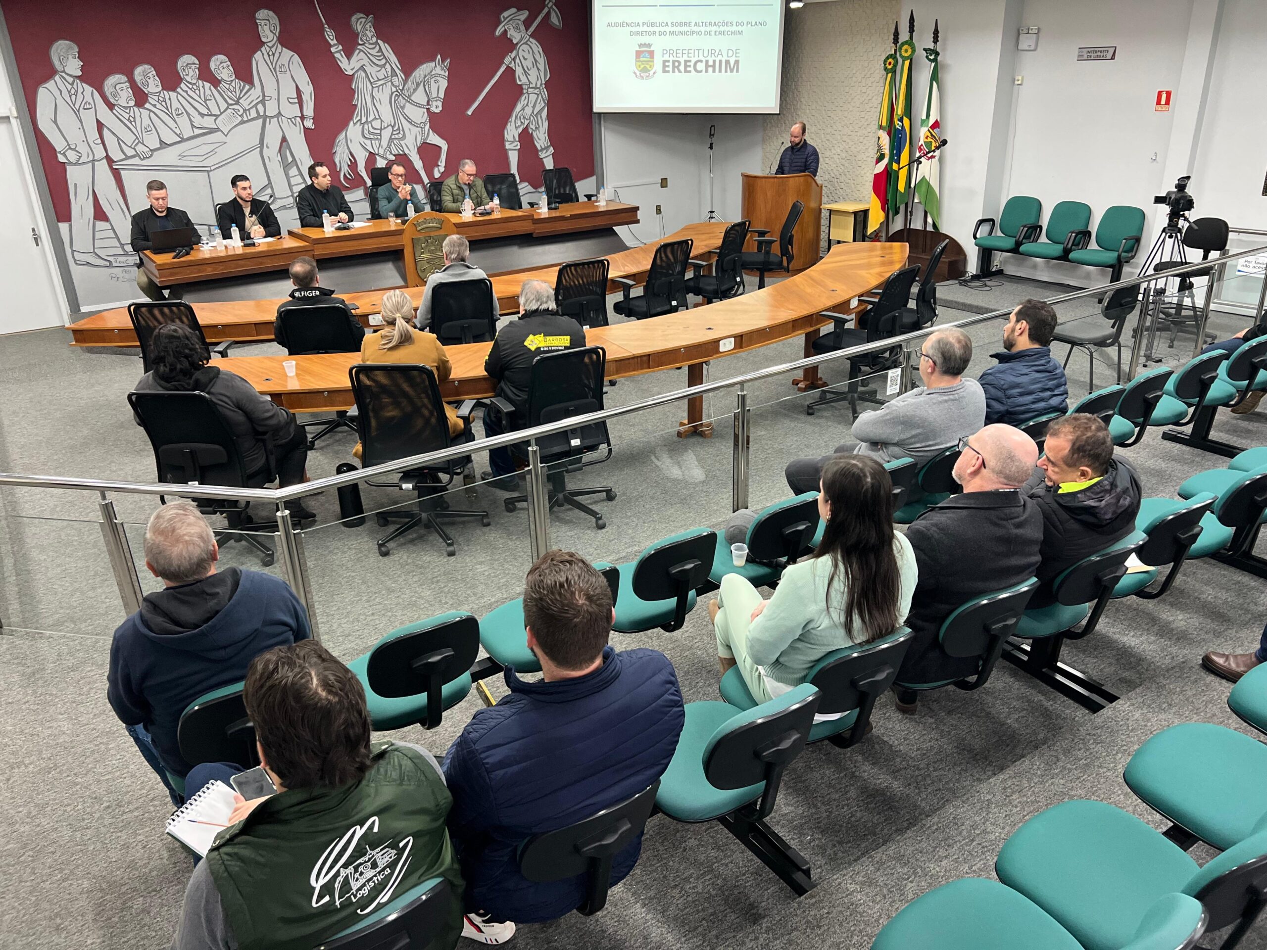 A Prefeitura de Erechim, por meio das secretarias de Obras, Habitação e Segurança Pública e de Desenvolvimento Econômico, Inovação e Turismo, realizou na manhã desta segunda-feira (22), na Câmara de Vereadores, a Audiência Pública de apresentação e discussão das propostas de alterações em eixos urbanos e zoneamento previstas no Plano Diretor do município. As mudanças em análise atendem demandas de empresas já instaladas em Erechim, que buscam ampliação de suas estruturas produtivas. O objetivo é compatibilizar o crescimento econômico com o planejamento urbano, fortalecendo a geração de empregos, a expansão da atividade industrial e o desenvolvimento sustentável do município. O Plano Diretor é o principal instrumento de planejamento urbano de Erechim, responsável por estabelecer diretrizes para o crescimento e desenvolvimento da cidade. A legislação define regras para o uso e ocupação do solo, organização dos bairros, mobilidade urbana, preservação ambiental, atividades econômicas e expansão urbana, buscando garantir um desenvolvimento equilibrado e sustentável. Por isso, qualquer alteração em eixos urbanos ou zoneamento exige análise técnica, debate com a comunidade e apreciação do Poder Legislativo.